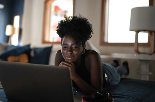 Menina está em seu quarto trabalhando com o laptop sobre a cama.