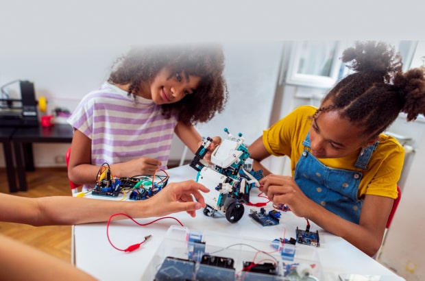 Crianças sentadas em uma mesa interagindo com equipamentos e construindo um robô
