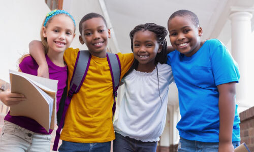 Imagem horizontal com visão frontal de grupo de alunos multirracial se abraçando.